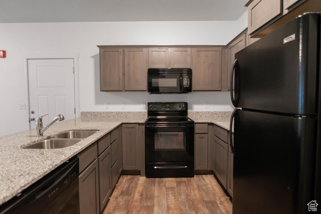 Kitchen with black appliances, light wood finished floors, light stone counters, and a peninsula