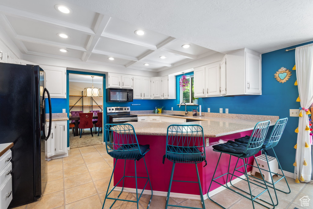 Kitchen with black appliances, a peninsula, coffered ceiling, white cabinetry, and recessed lighting