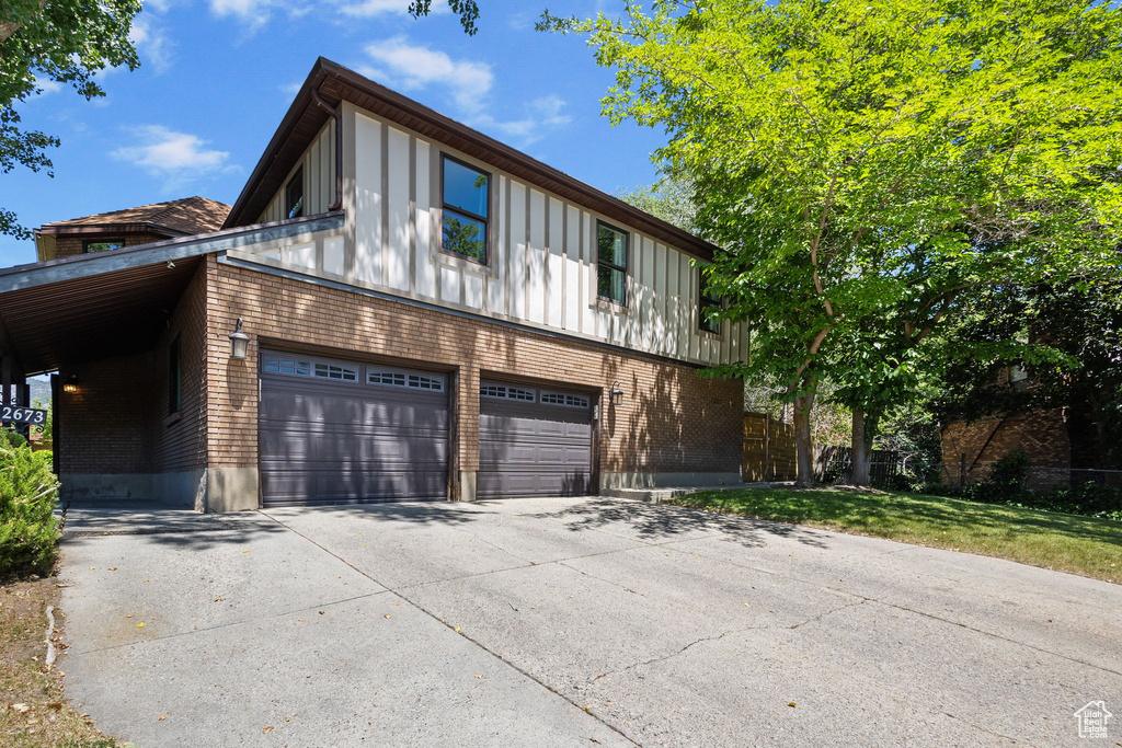 View of front of house featuring driveway, a garage, brick siding, board and batten siding, and a front yard