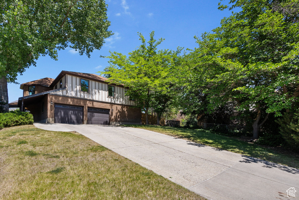 View of front of home featuring an attached garage, driveway, board and batten siding, and brick siding