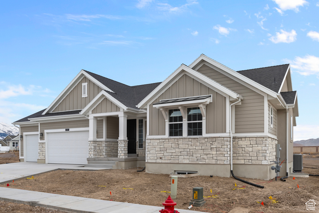 Craftsman-style home with stone siding, board and batten siding, concrete driveway, a porch, and a shingled roof