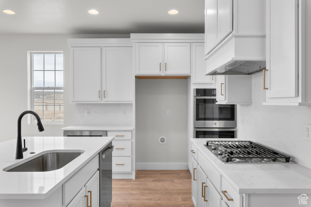 Kitchen featuring stainless steel appliances, recessed lighting, tasteful backsplash, light wood-style flooring, and white cabinetry