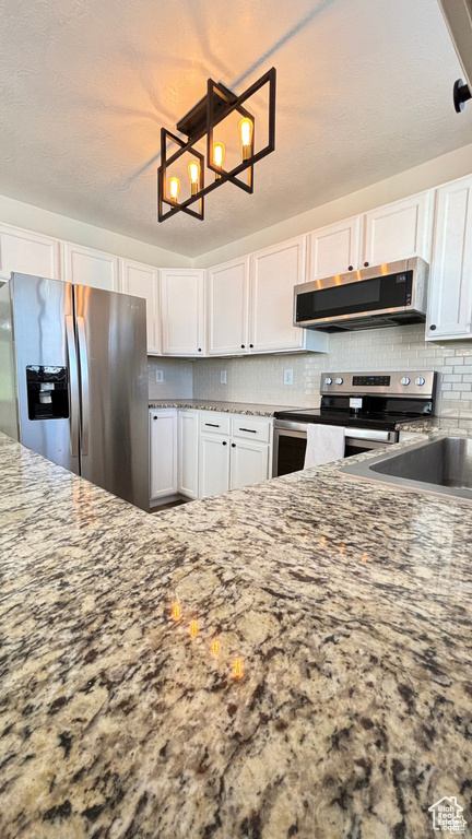 Kitchen with stone countertops, white cabinetry, and appliances with stainless steel finishes