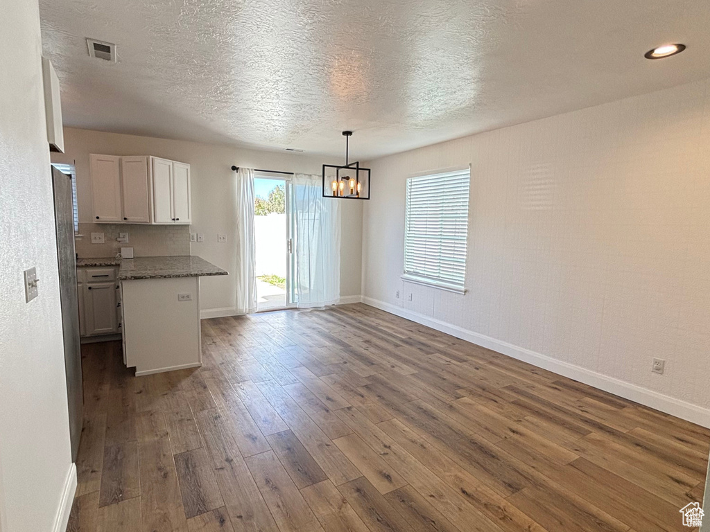 Interior space with dark hardwood / wood-style flooring, dark stone countertops, pendant lighting, a textured ceiling, and white cabinets
