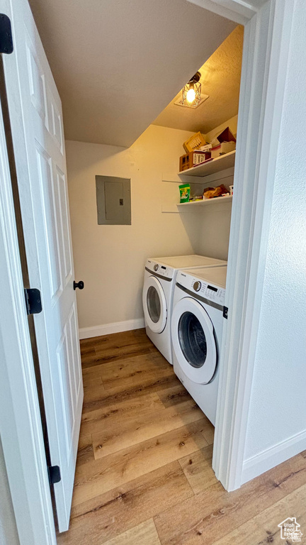 Washroom featuring electric panel, washer and clothes dryer, and light hardwood / wood-style flooring