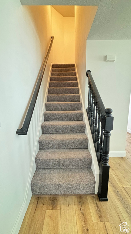 Stairs featuring hardwood / wood-style floors and a textured ceiling