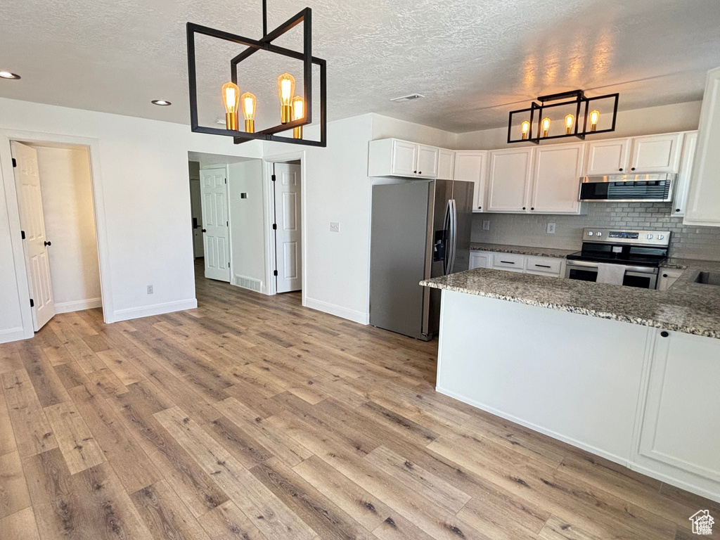 Kitchen featuring an inviting chandelier, white cabinets, appliances with stainless steel finishes, decorative light fixtures, and extractor fan