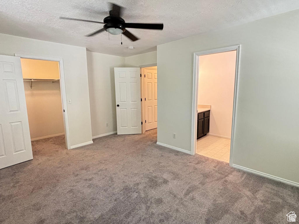 Unfurnished bedroom featuring light carpet, a walk in closet, ceiling fan, connected bathroom, and a closet