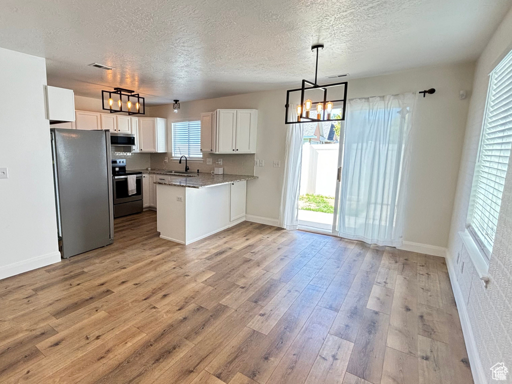 Kitchen featuring appliances with stainless steel finishes, light stone counters, sink, a notable chandelier, and white cabinetry
