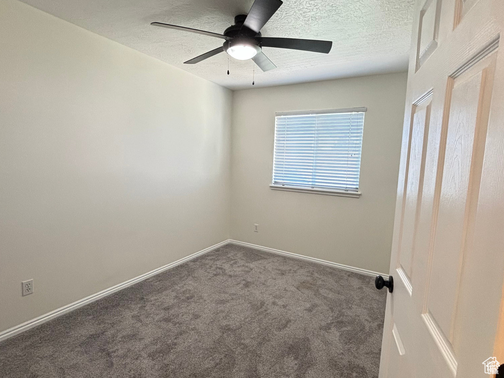 Unfurnished room with dark colored carpet, a textured ceiling, and ceiling fan