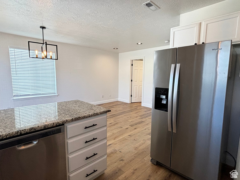 Kitchen with white cabinets, stainless steel appliances, hanging light fixtures, and a chandelier