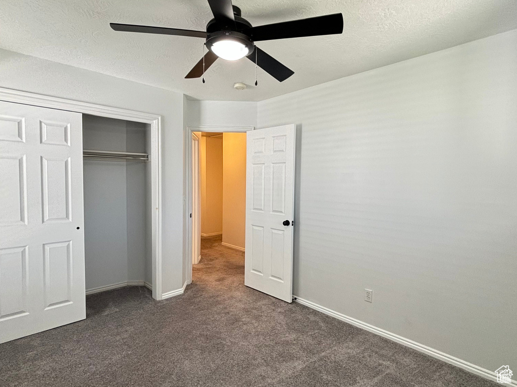 Unfurnished bedroom with dark colored carpet, ceiling fan, and a closet