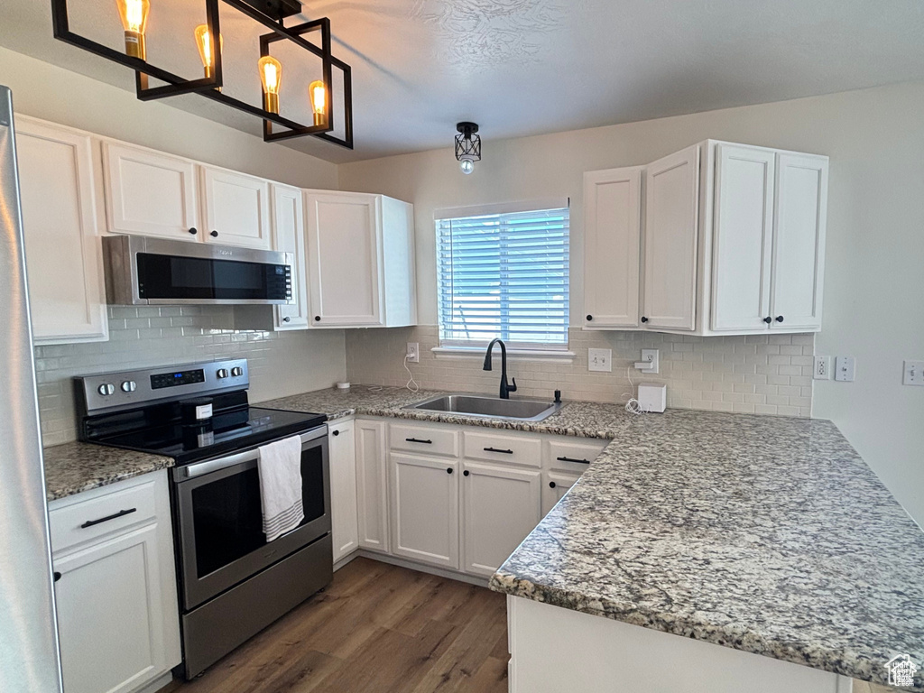 Kitchen with kitchen peninsula, appliances with stainless steel finishes, light stone countertops, sink, and white cabinets