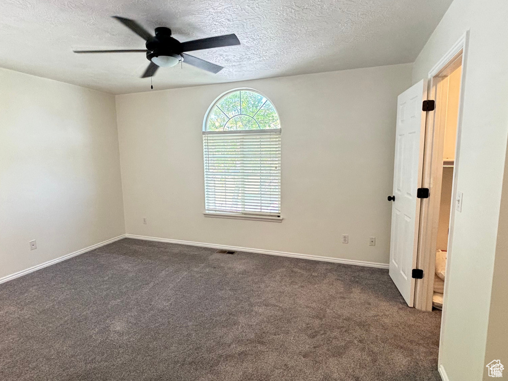 Empty room featuring ceiling fan, a textured ceiling, and dark colored carpet