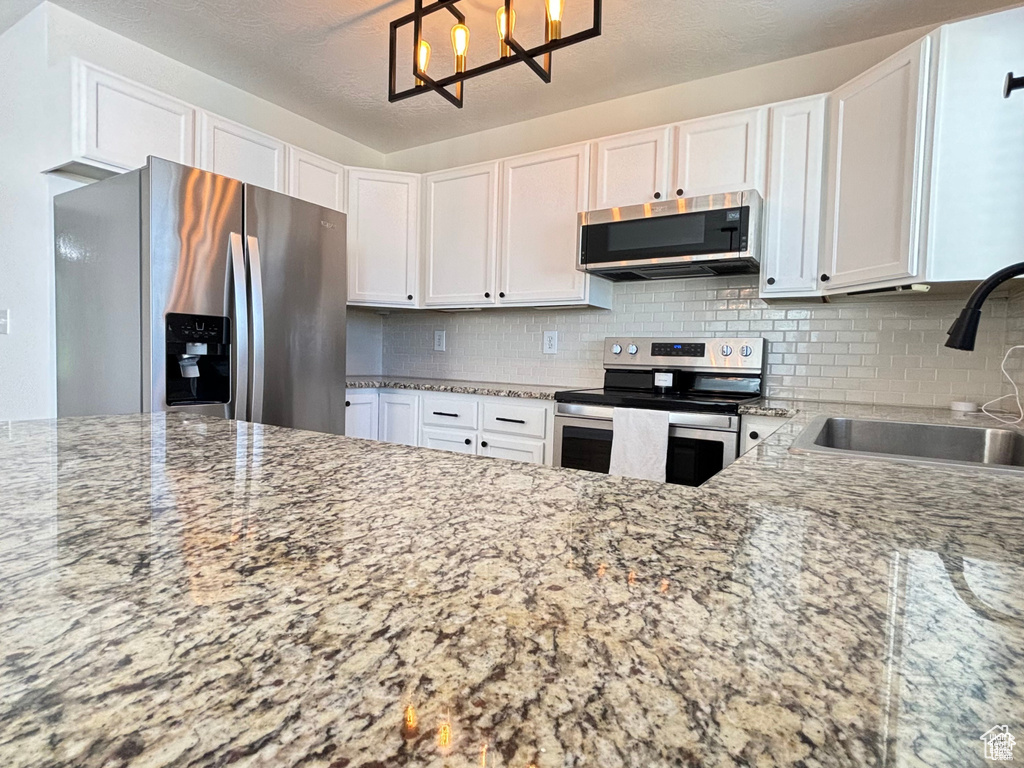 Kitchen featuring backsplash, white cabinets, sink, appliances with stainless steel finishes, and light stone counters