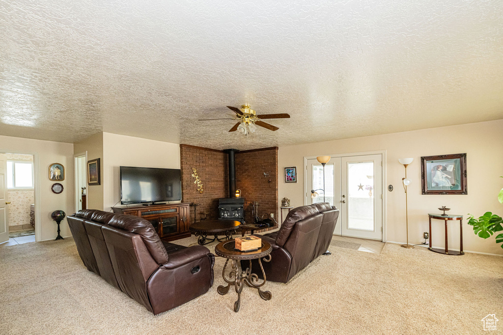 Living room with a wood stove, light carpet, ceiling fan, a textured ceiling, and french doors