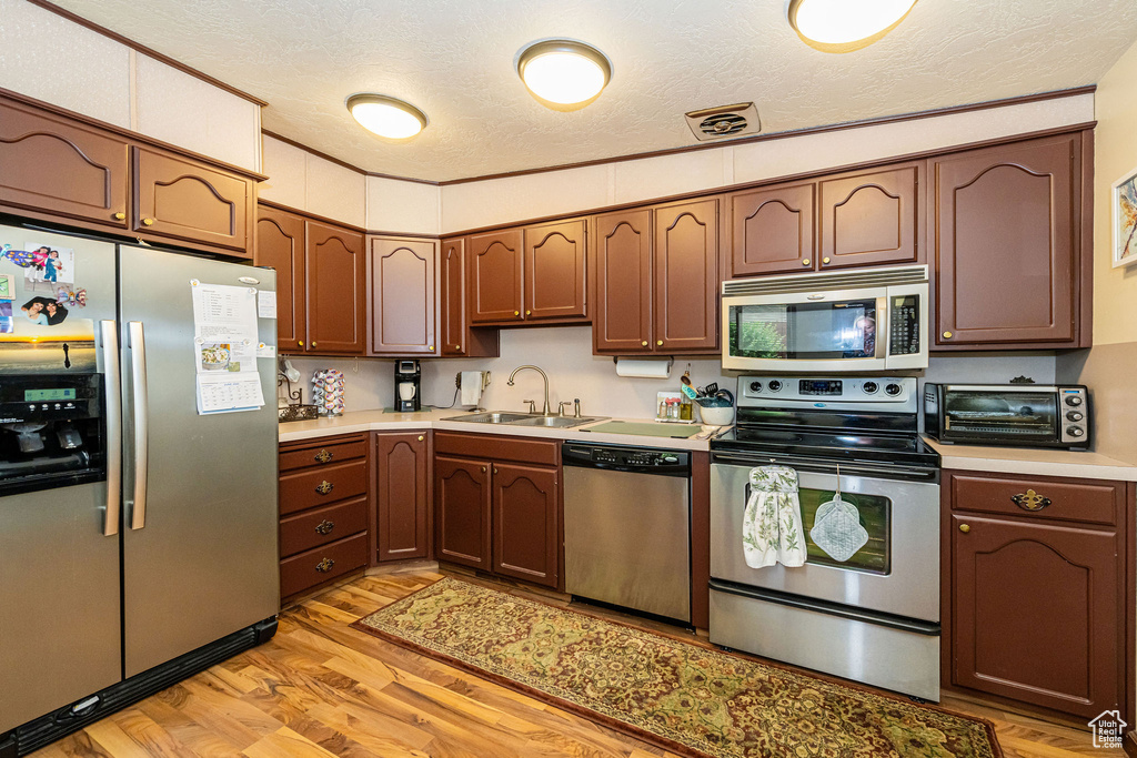 Kitchen featuring appliances with stainless steel finishes, light wood finished floors, a textured ceiling, and light countertops