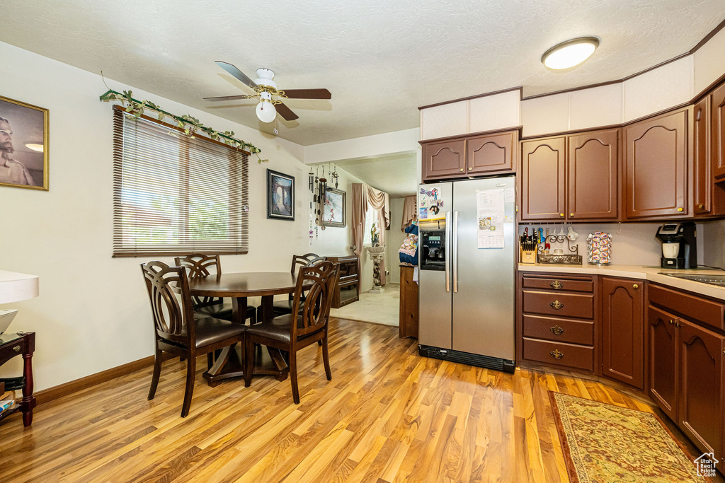 Kitchen with stainless steel refrigerator with ice dispenser, light wood-style floors, a ceiling fan, light countertops, and plenty of natural light