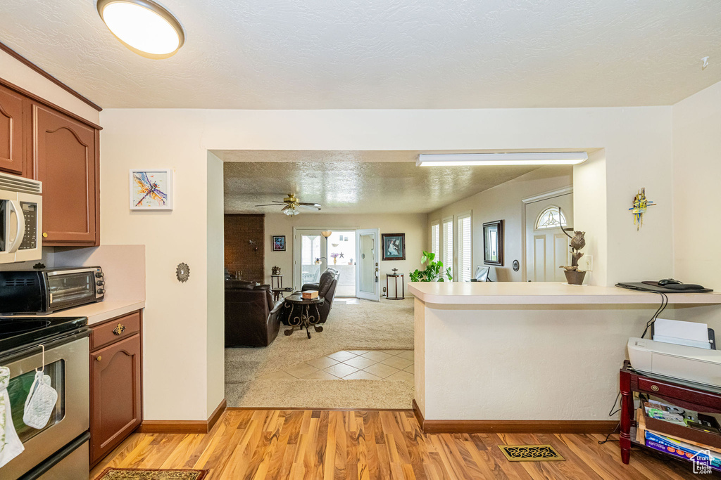 Kitchen featuring stainless steel electric stove, white microwave, open floor plan, light countertops, and a peninsula