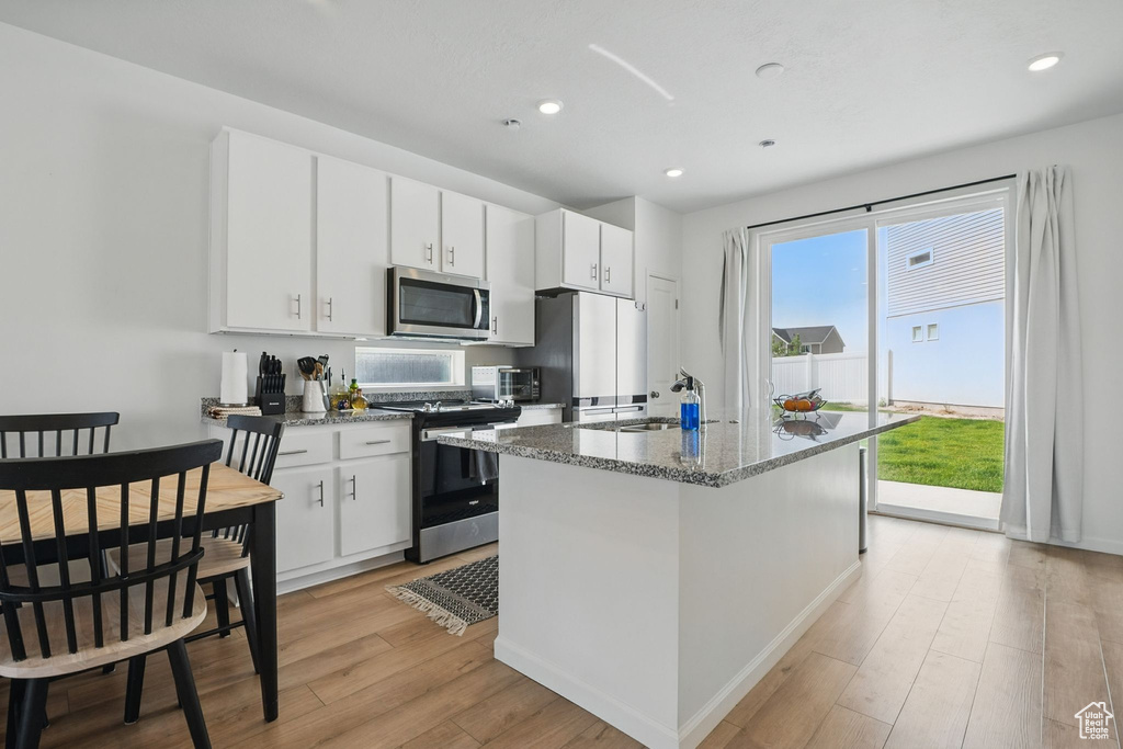 Kitchen with stainless steel microwave, gas range oven, freestanding refrigerator, light wood-style flooring, and a kitchen island with sink