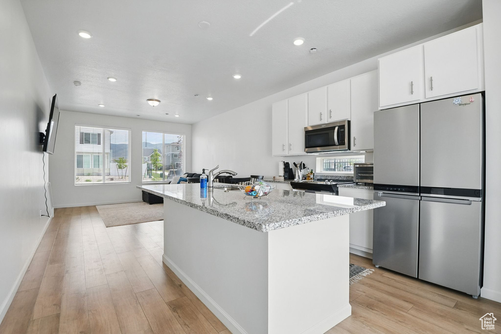 Kitchen featuring appliances with stainless steel finishes, an island with sink, recessed lighting, light wood finished floors, and white cabinetry