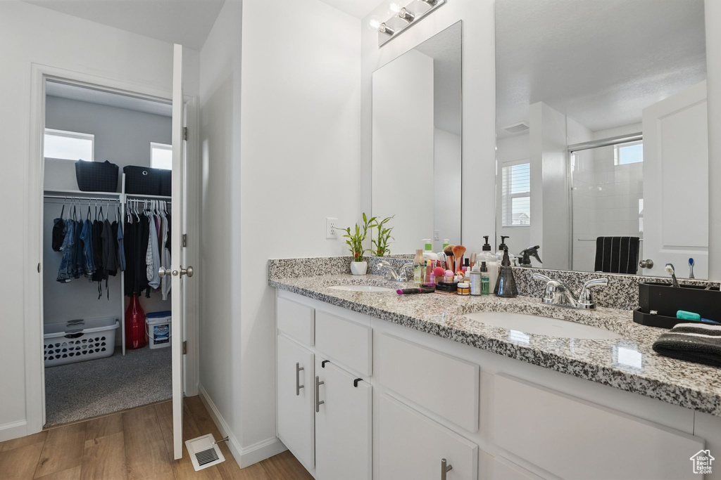 Bathroom with wood finished floors, a shower stall, double vanity, and a walk in closet