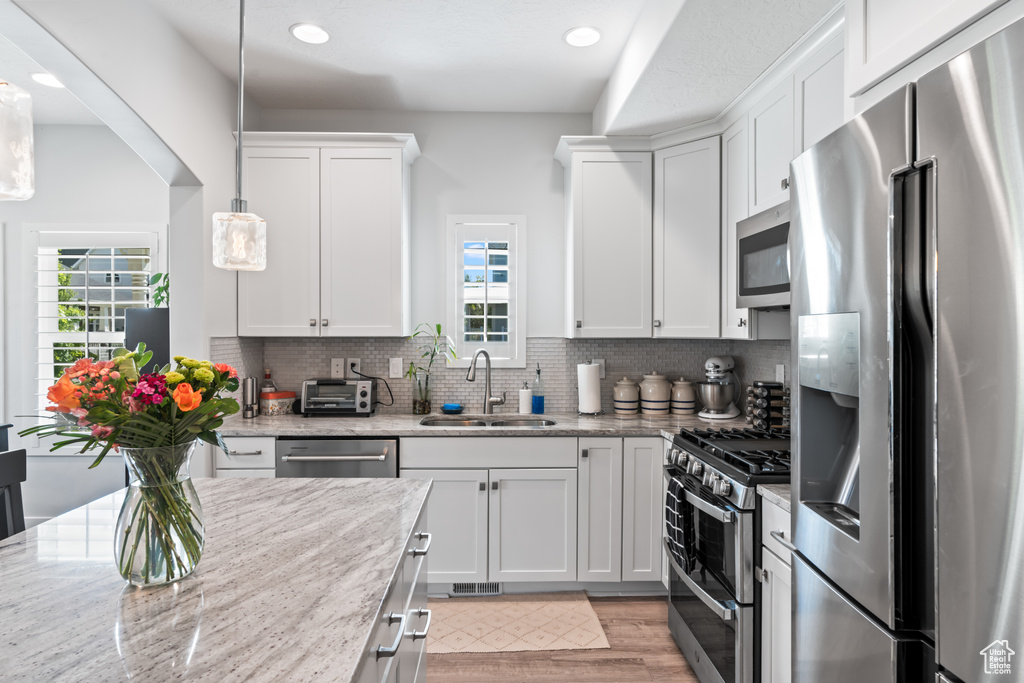 Kitchen with stainless steel appliances, white cabinets, plenty of natural light, light wood-type flooring, and recessed lighting