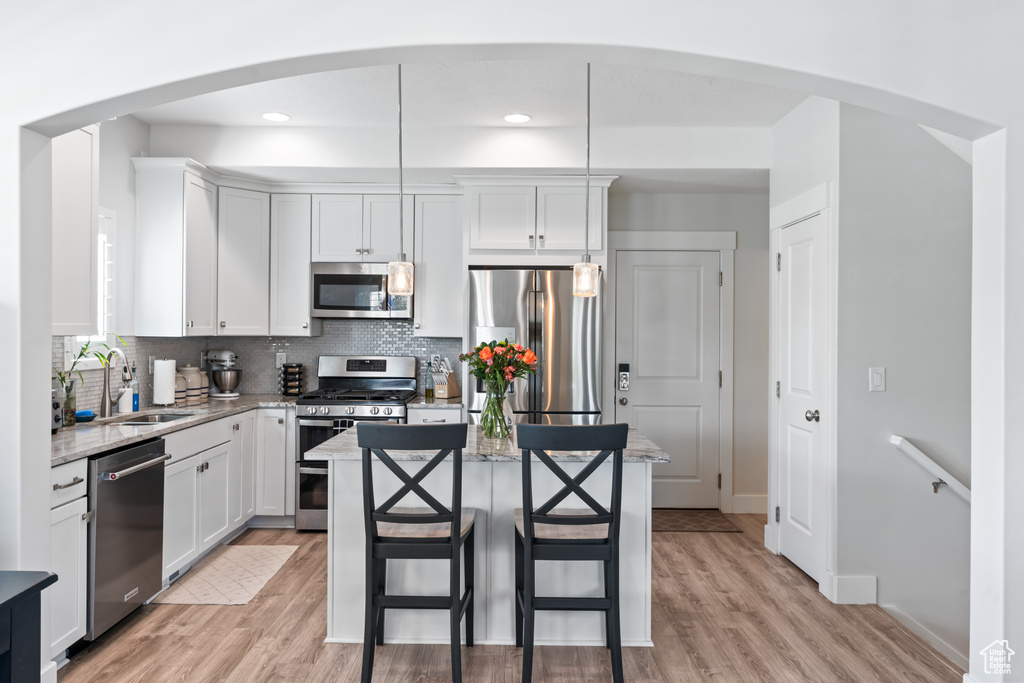 Kitchen featuring appliances with stainless steel finishes, arched walkways, a kitchen island, light wood finished floors, and backsplash