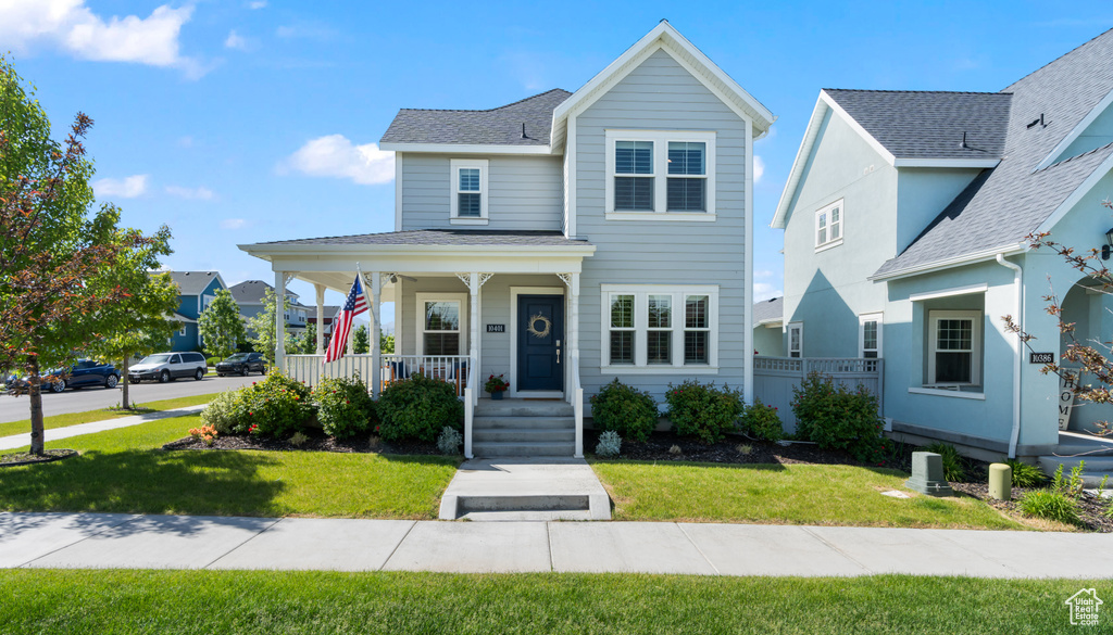 Traditional-style house featuring a porch, a front lawn, and a shingled roof