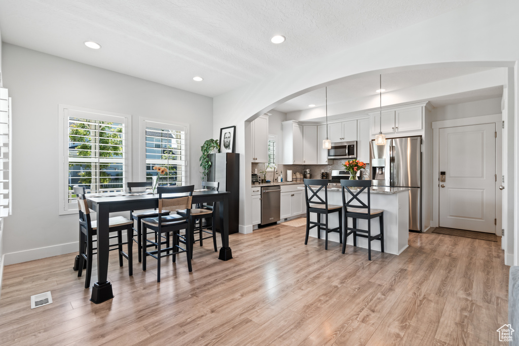 Dining space with light wood-style flooring, arched walkways, and recessed lighting