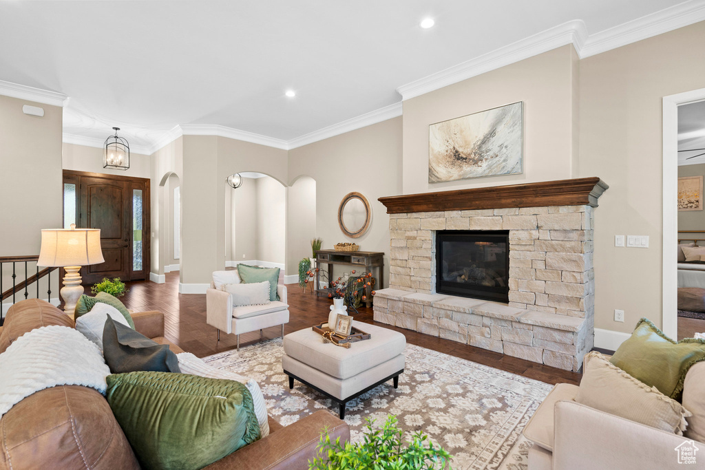 Living room featuring arched walkways, ornamental molding, wood finished floors, recessed lighting, and a stone fireplace