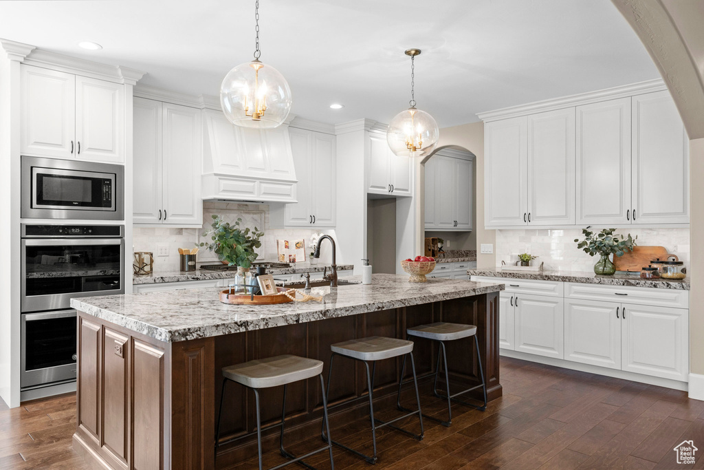 Kitchen featuring appliances with stainless steel finishes, decorative backsplash, dark wood finished floors, arched walkways, and recessed lighting