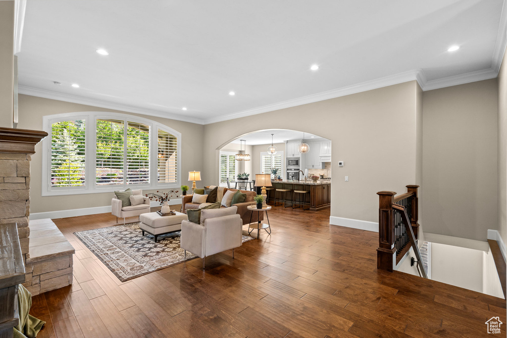 Living area featuring arched walkways, dark wood-type flooring, crown molding, and recessed lighting