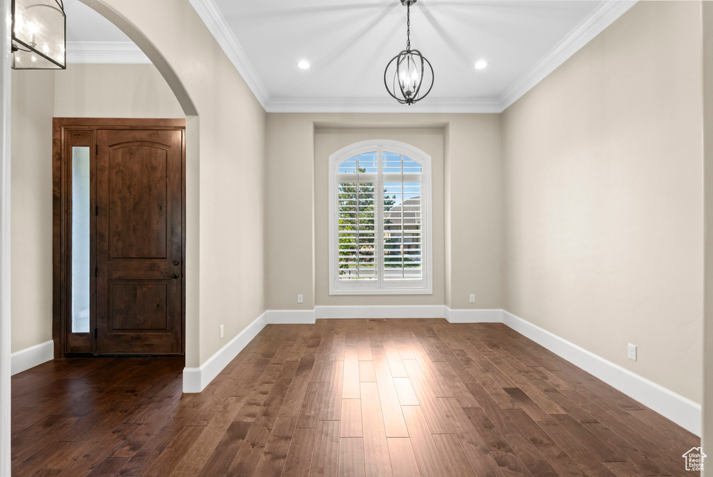 Foyer featuring a chandelier, dark wood finished floors, crown molding, arched walkways, and recessed lighting