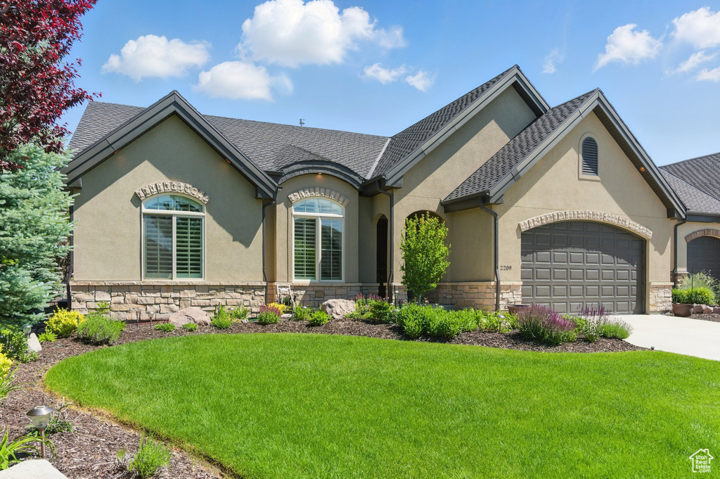 French country home featuring stone siding, stucco siding, an attached garage, a front yard, and driveway
