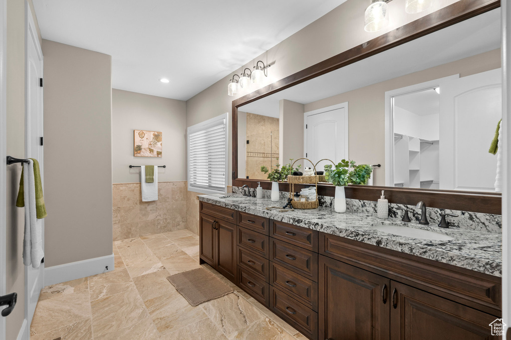 Full bathroom featuring double vanity, a tile shower, and a wainscoted wall