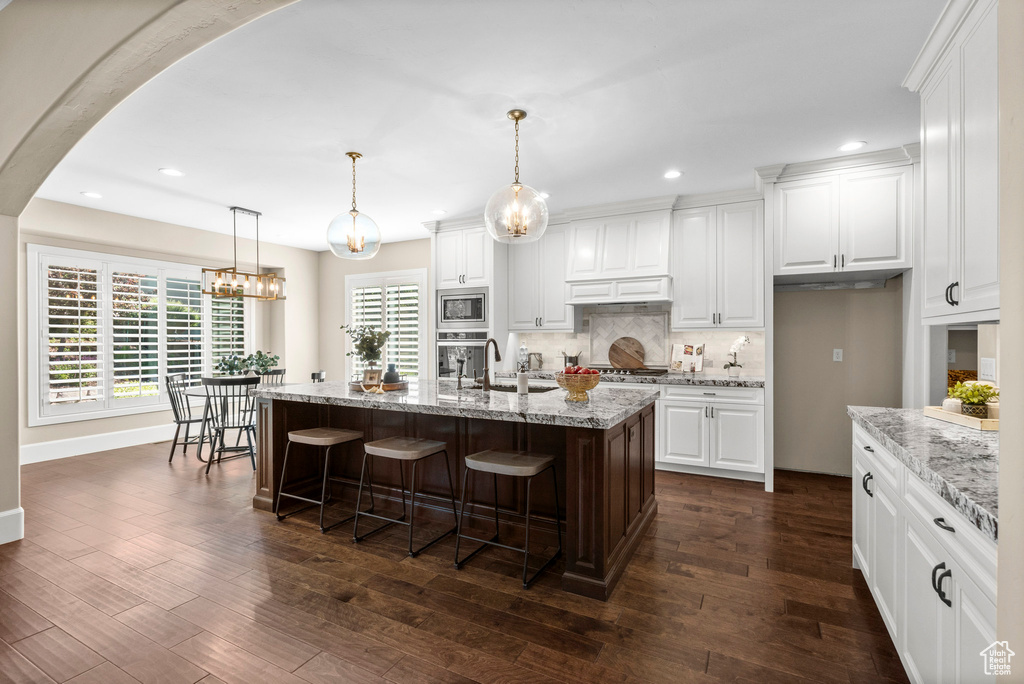 Kitchen with appliances with stainless steel finishes, recessed lighting, decorative backsplash, white cabinets, and a breakfast bar area