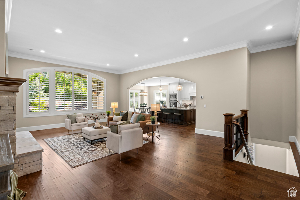 Living room with arched walkways, dark wood-style floors, crown molding, and recessed lighting