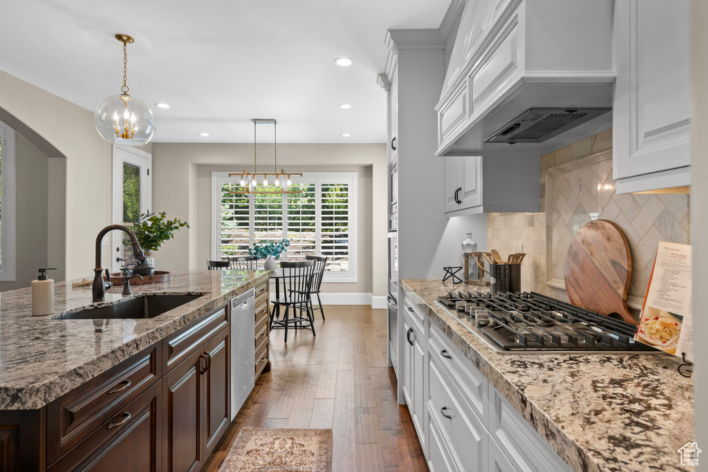 Kitchen featuring appliances with stainless steel finishes, custom range hood, arched walkways, a chandelier, and dark brown cabinetry