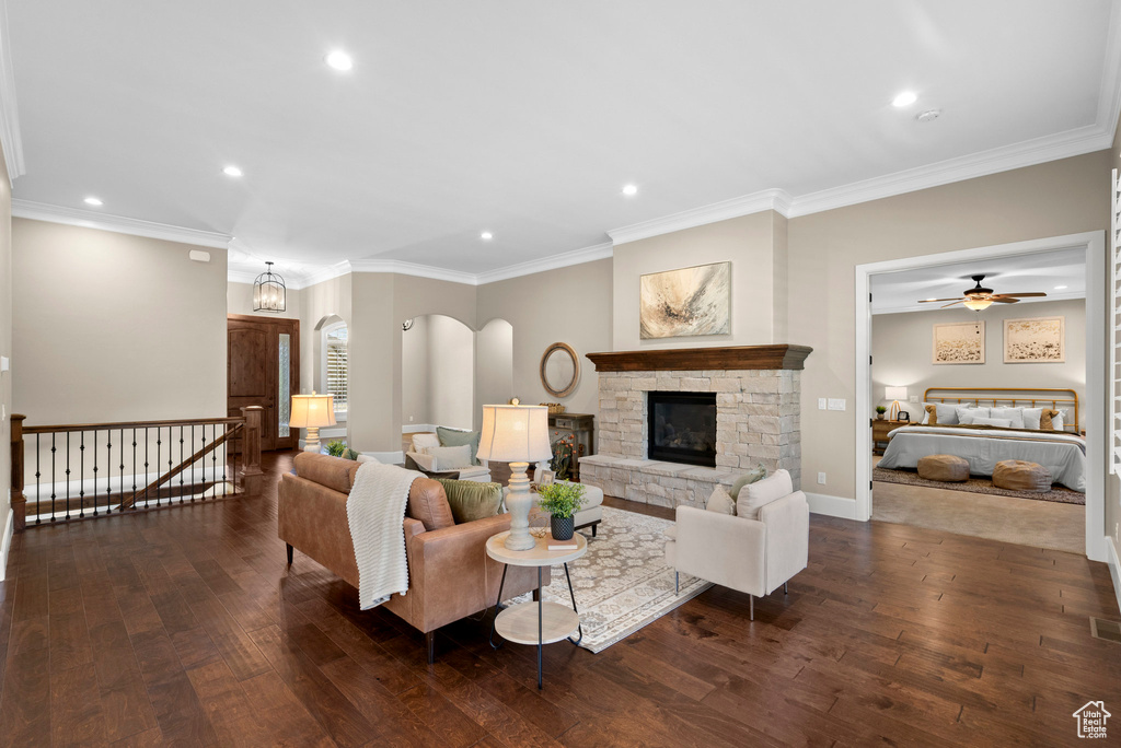 Living area featuring dark wood-type flooring, recessed lighting, crown molding, a stone fireplace, and arched walkways