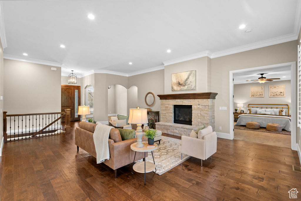 Living area with recessed lighting, dark wood-style floors, a stone fireplace, ornamental molding, and a ceiling fan