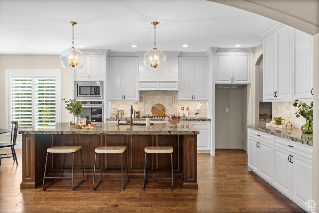 Kitchen featuring stainless steel appliances, recessed lighting, a kitchen breakfast bar, arched walkways, and white cabinets