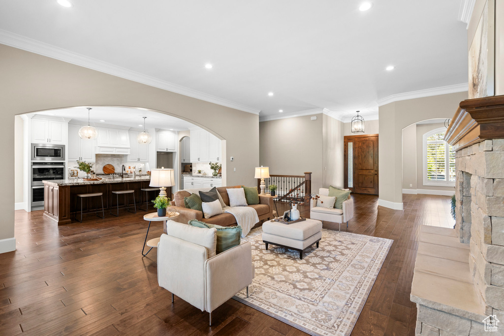 Living room with arched walkways, recessed lighting, dark wood finished floors, and crown molding