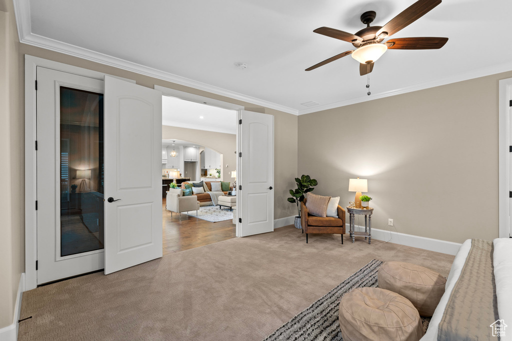 Sitting room with light colored carpet, crown molding, ceiling fan, and arched walkways