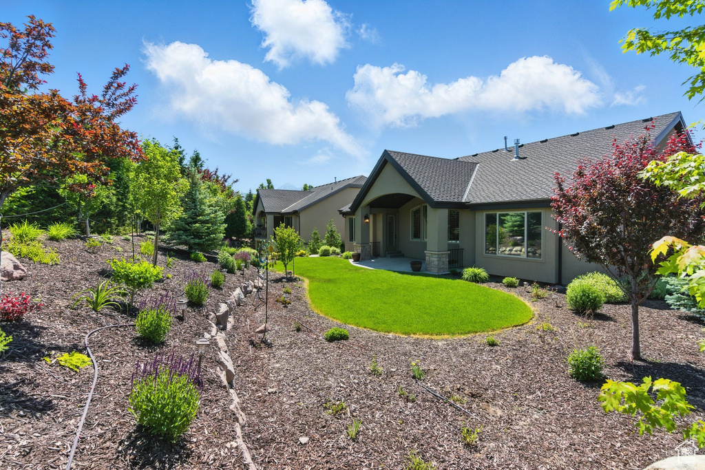 Rear view of house with stucco siding, a lawn, and a shingled roof