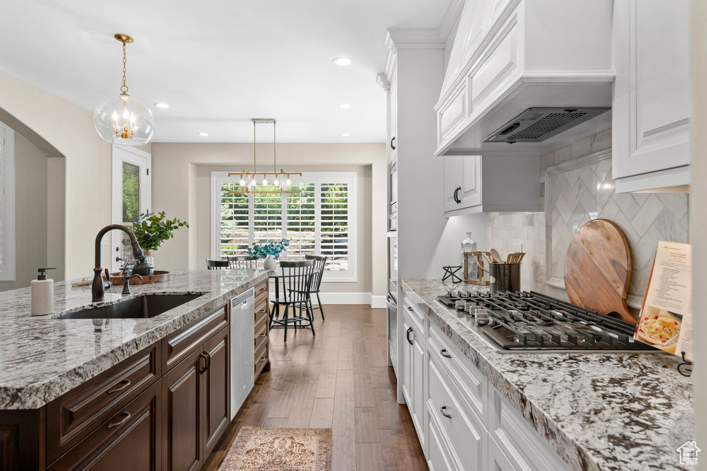 Kitchen featuring stainless steel appliances, custom exhaust hood, arched walkways, white cabinets, and recessed lighting