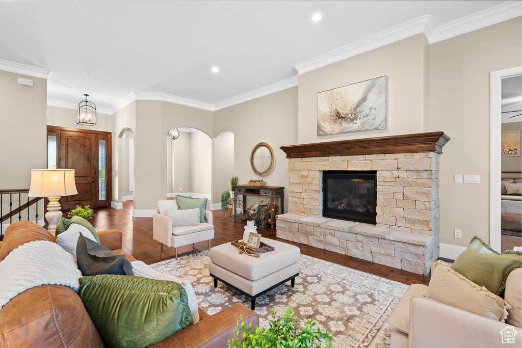 Living room featuring arched walkways, ornamental molding, recessed lighting, wood finished floors, and a stone fireplace