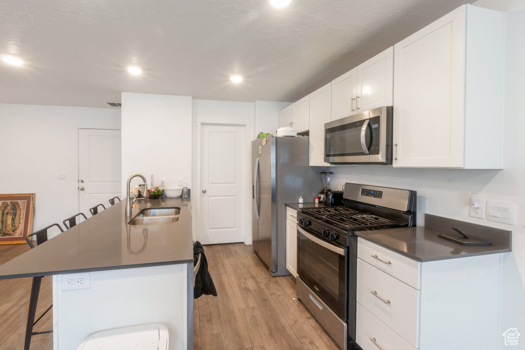 Kitchen with stainless steel appliances, a kitchen bar, light wood finished floors, white cabinetry, and recessed lighting