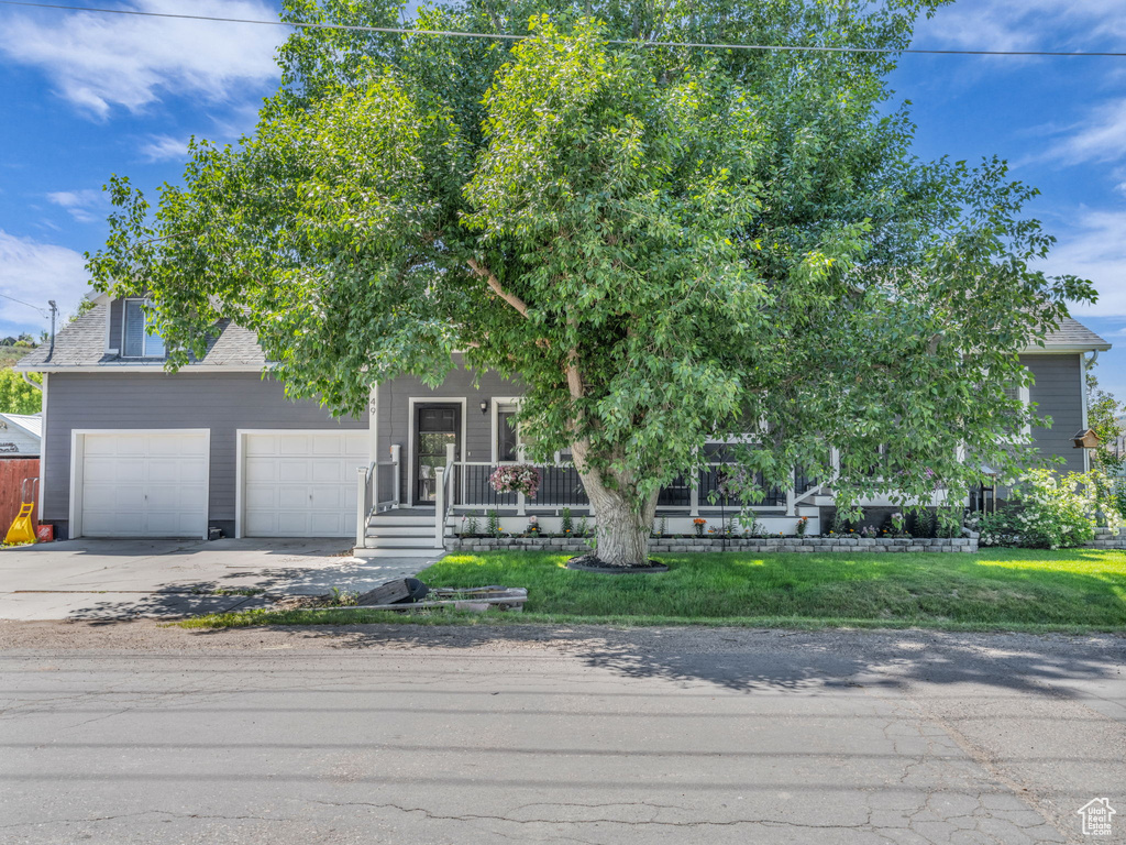 Obstructed view of property featuring driveway, a garage, covered porch, a front yard, and roof with shingles