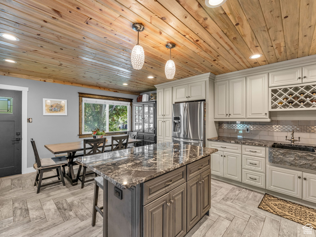 Kitchen with stainless steel fridge, wood ceiling, recessed lighting, dark stone countertops, and a kitchen breakfast bar